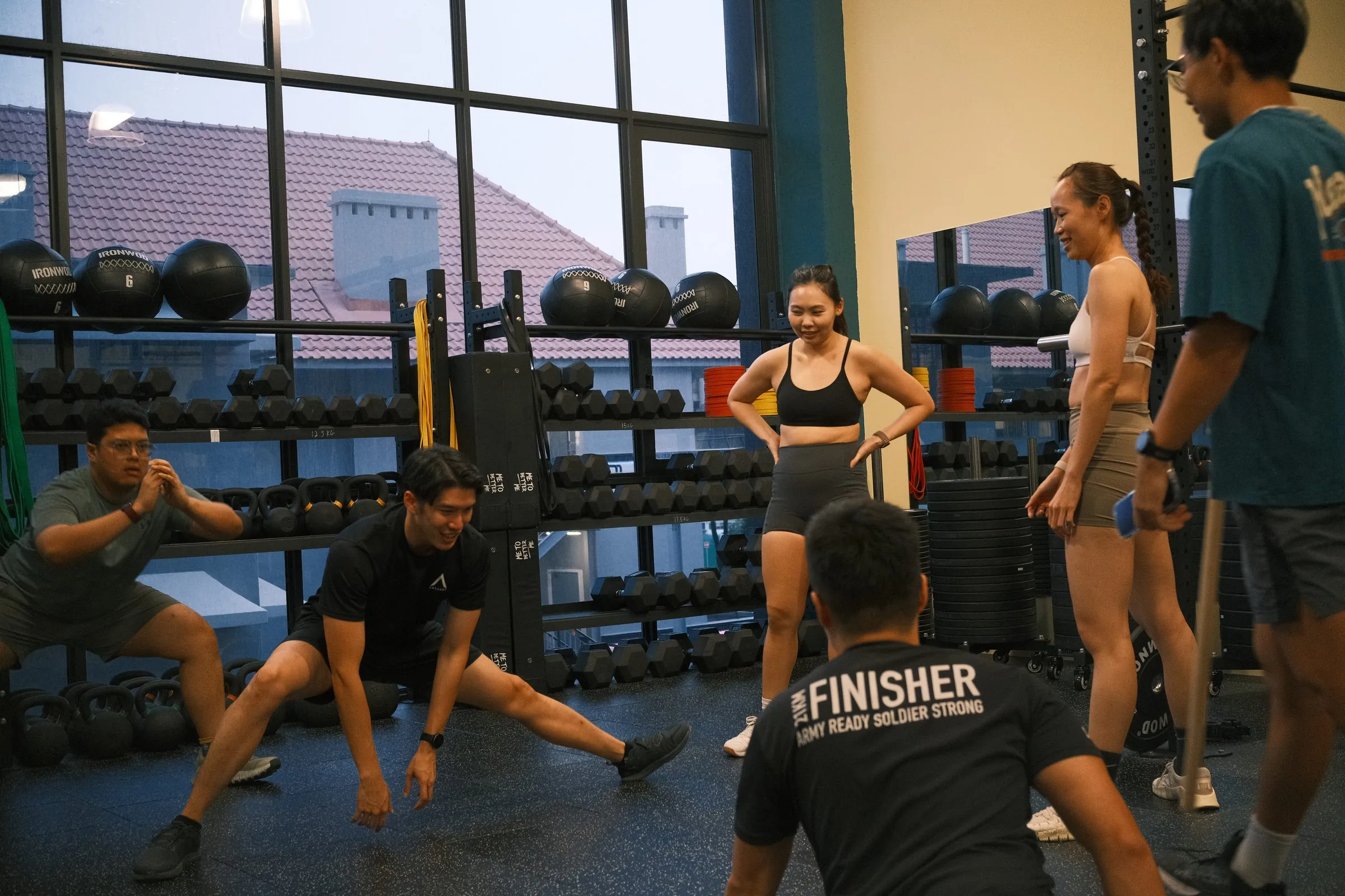 A coach leading the warm-up, members stretching by the dumbbell rack.