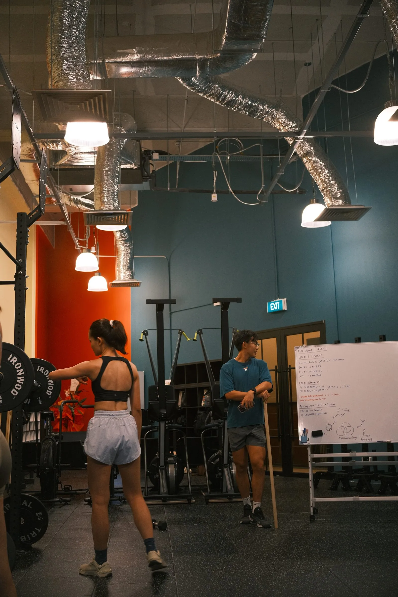 A coach by the whiteboard, talking a member through the day’s session.